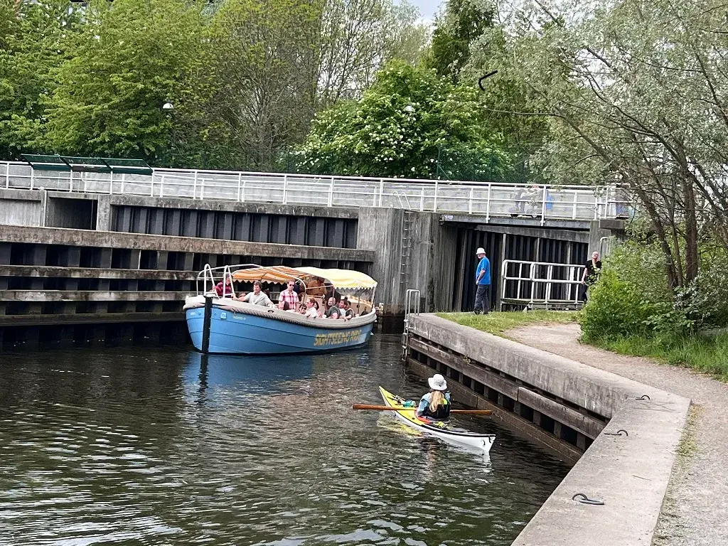Sightseeing Rides blå eldrivna båt med gäster i Sicklaslussen, med en kajakpaddlare i förgrunden