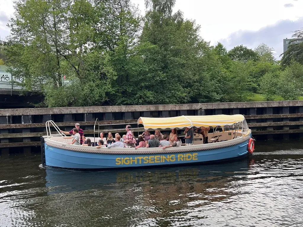 Sightseeing Rides båt full av gäster under det gulrandiga soltaket på vattnet vid Hammarby Sjöstad