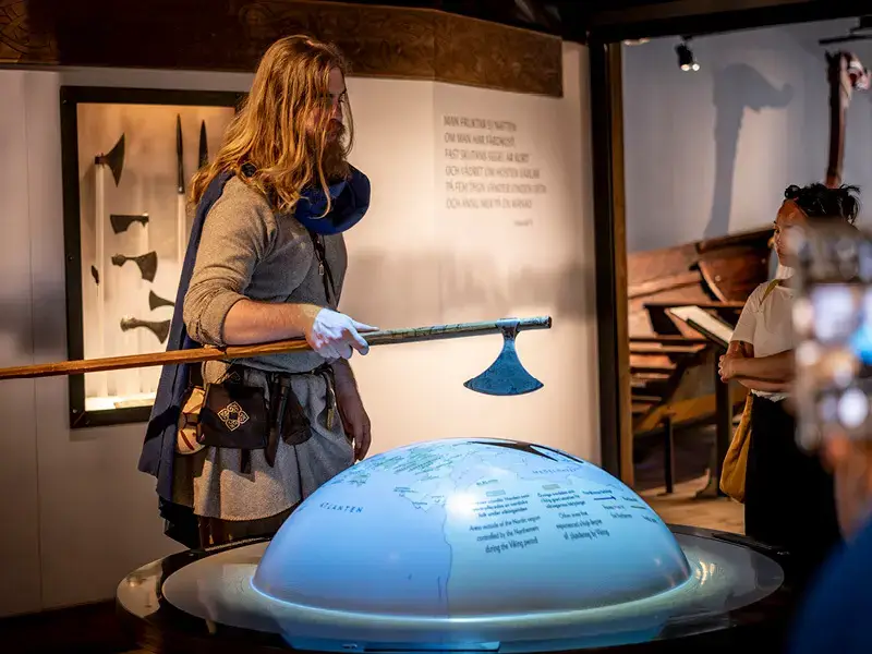 Guide in Viking costume presenting with an axe by a map of the Viking world at the Viking Museum in Stockholm