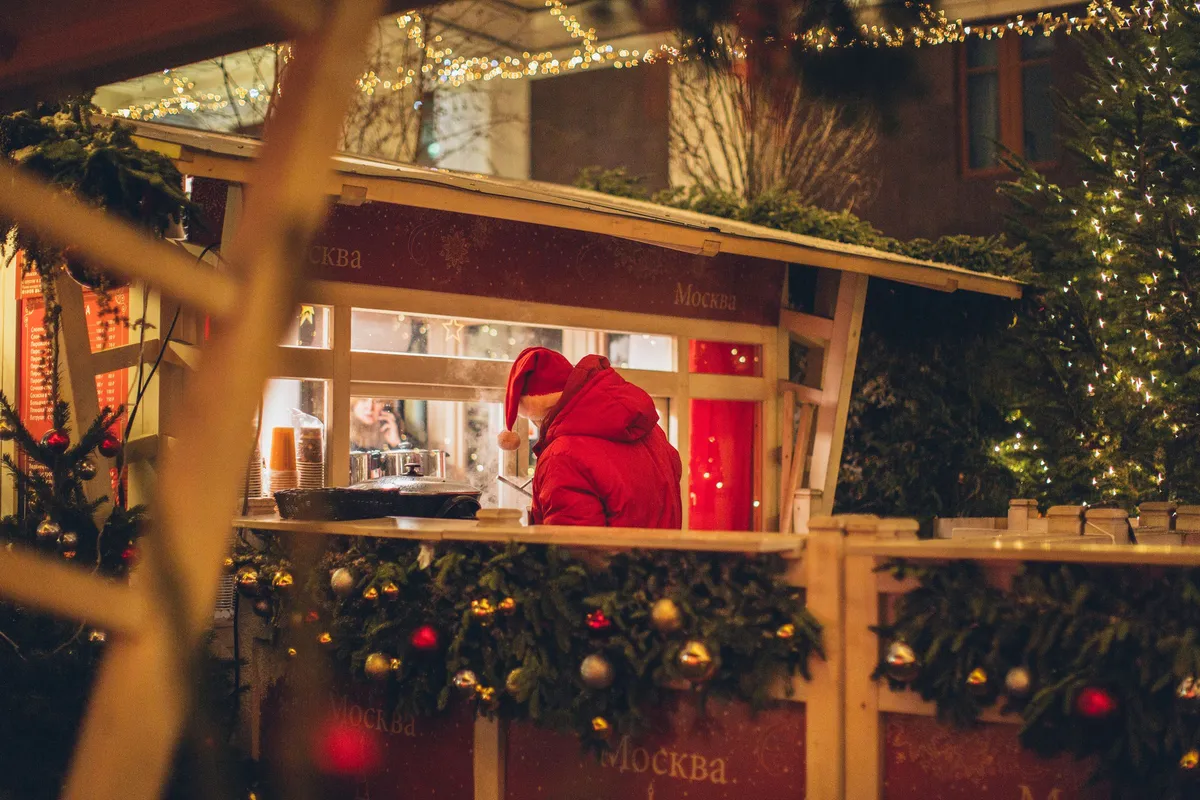 Besökare köper en varm dryck vid ett upplyst julmarknadsstånd