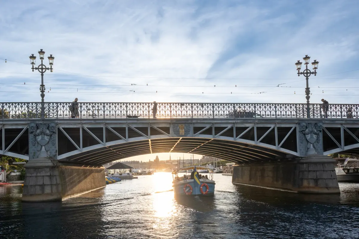 Öppen sightseeingbåt som passerar under en låg bro i Stockholm