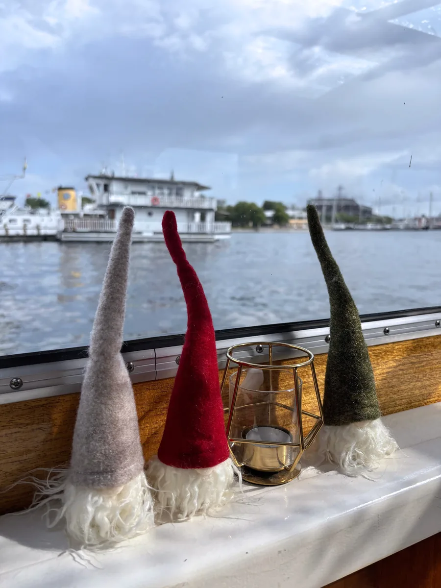 Swedish tomte figures and a lantern on the cabin windowsill with the water behind them