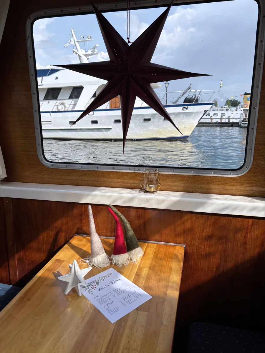A Christmas star hanging in the cabin window with a boat and the water outside, and the winter menu on the table