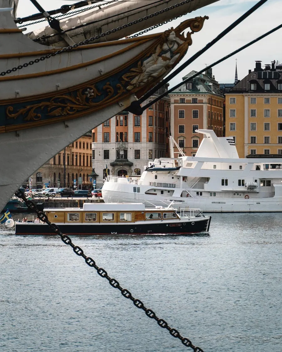 Sightseeing Rides klassiska elbåt passerar de ockragula fasaderna vid Skeppsbron i Gamla stan i Stockholm