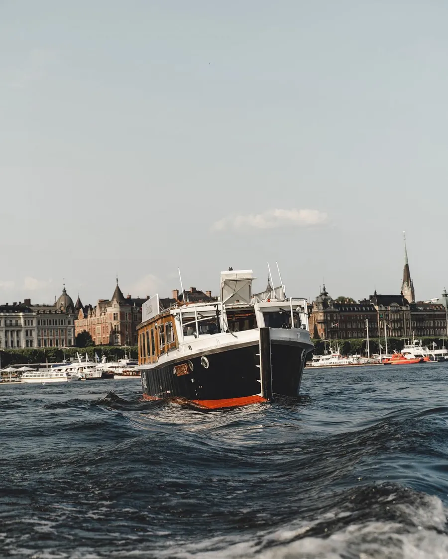 Sightseeing Rides klassiska elbåt på vattnet med Strandvägens fasader och Oscarskyrkans torn bakom sig i Stockholm